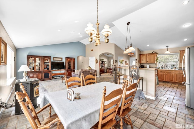 dining space with vaulted ceiling, stone tile floors, recessed lighting, an inviting chandelier, and arched walkways