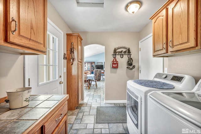 clothes washing area featuring arched walkways, cabinet space, washer and clothes dryer, and stone finish floor