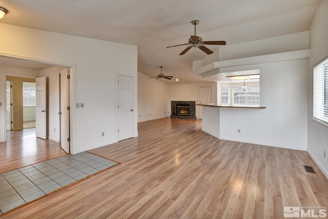 unfurnished living room featuring visible vents, light wood-style flooring, a lit fireplace, ceiling fan, and vaulted ceiling