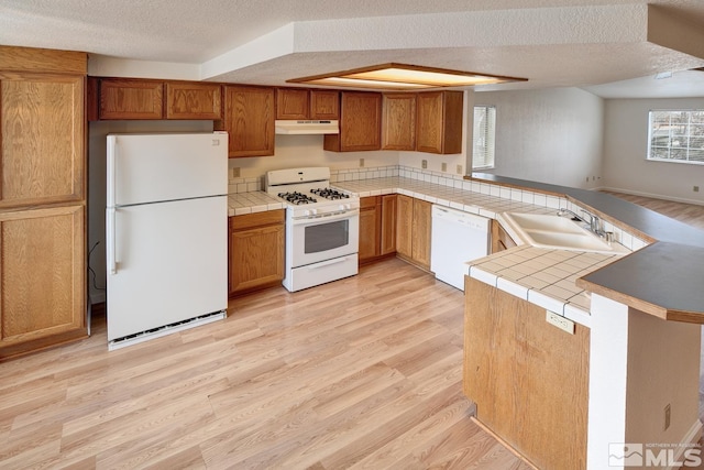 kitchen with light wood-style flooring, under cabinet range hood, a sink, white appliances, and a peninsula