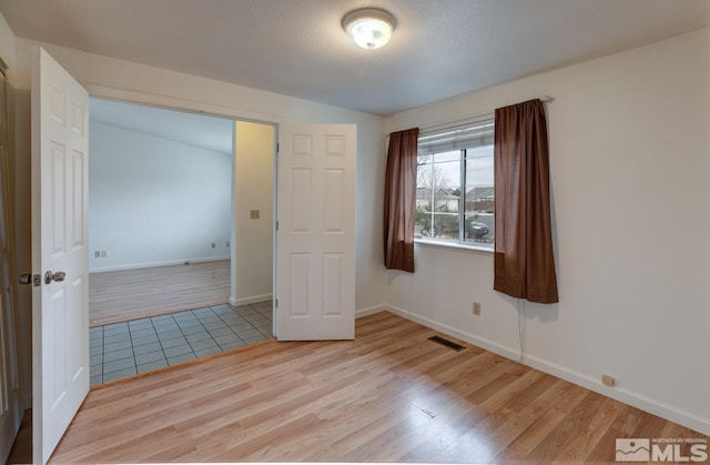 spare room with a textured ceiling, wood finished floors, visible vents, and baseboards