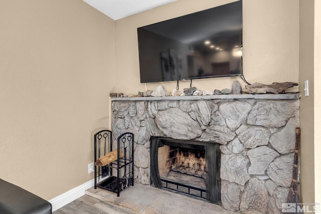 interior details featuring baseboards, a stone fireplace, and wood finished floors