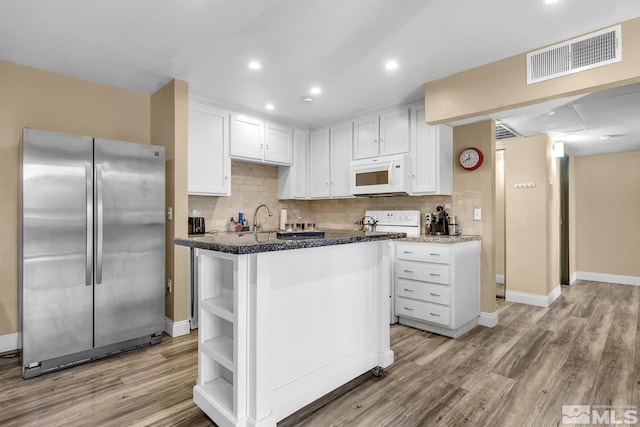 kitchen with white microwave, visible vents, open shelves, freestanding refrigerator, and white cabinetry