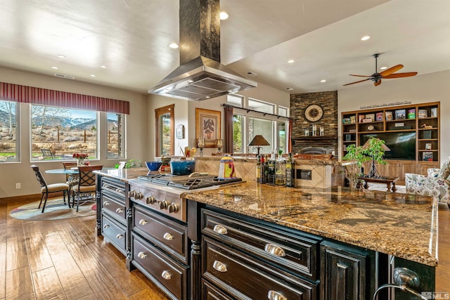 kitchen with island range hood, open floor plan, stone counters, hardwood / wood-style flooring, and stainless steel gas stovetop