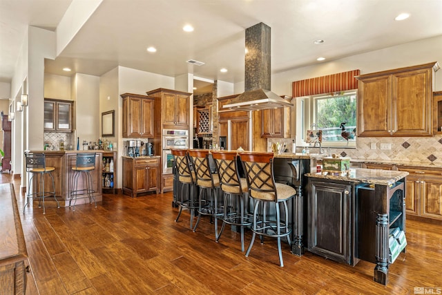 kitchen with brown cabinets, a breakfast bar, a kitchen island, dark wood finished floors, and island range hood