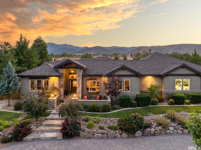 view of front of house with a front yard, a mountain view, stone siding, and stucco siding