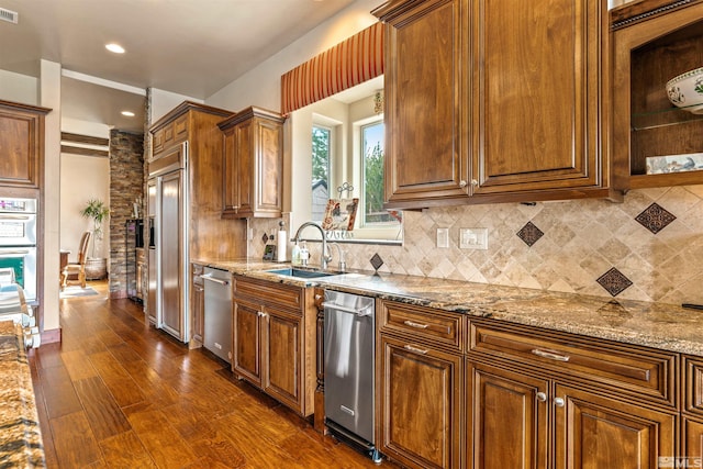 kitchen with light stone counters, dark wood-style flooring, backsplash, and a sink