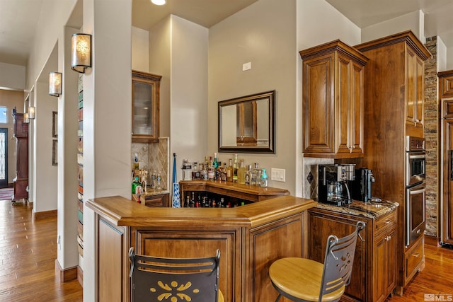 bar with wood finished floors, baseboards, a bar, double oven, and backsplash