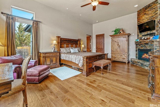 bedroom with a ceiling fan, a towering ceiling, a fireplace, and light wood finished floors