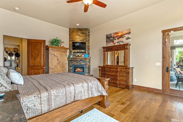 bedroom with baseboards, a stone fireplace, light wood-style flooring, and a ceiling fan