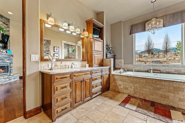 full bath featuring a garden tub, stone tile floors, a fireplace, a chandelier, and vanity