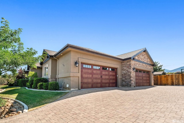 view of side of home featuring stucco siding, decorative driveway, stone siding, fence, and an attached garage