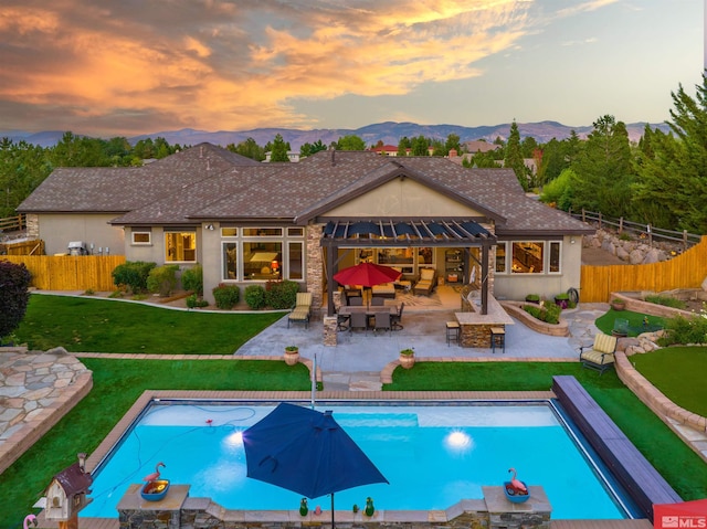 pool at dusk with a lawn, outdoor dry bar, a patio, fence, and a mountain view