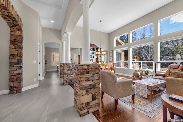 living area with decorative columns, baseboards, an inviting chandelier, and a towering ceiling