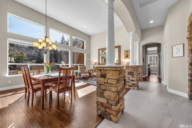 dining area with baseboards, a towering ceiling, arched walkways, a notable chandelier, and ornate columns