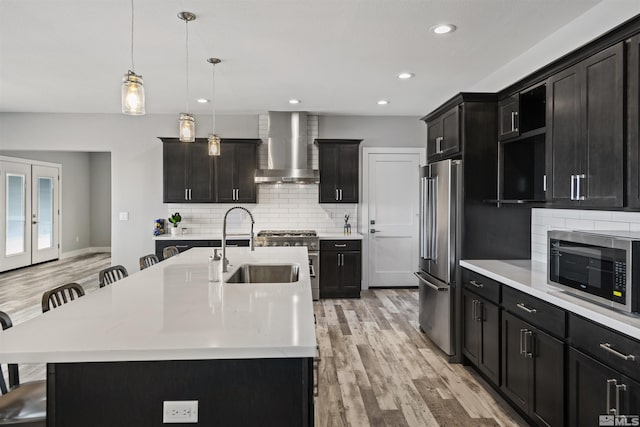 kitchen with an island with sink, a sink, light countertops, wall chimney range hood, and high quality appliances