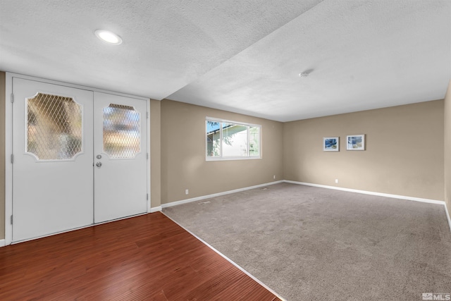 carpeted foyer entrance featuring wood finished floors, baseboards, french doors, and a textured ceiling