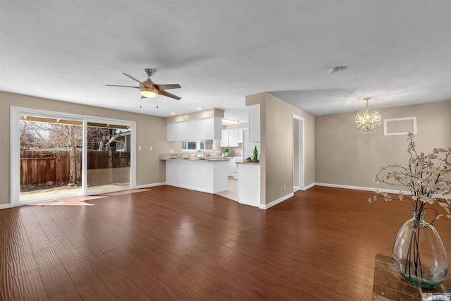 unfurnished living room featuring ceiling fan with notable chandelier, baseboards, and wood finished floors