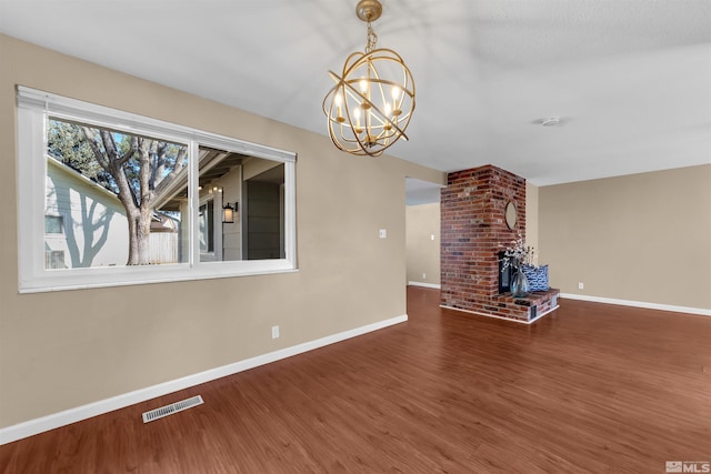 unfurnished living room featuring visible vents, wood finished floors, an inviting chandelier, a fireplace, and baseboards