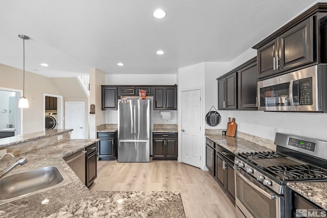 kitchen with light stone counters, washer / dryer, a sink, stainless steel appliances, and light wood-style floors