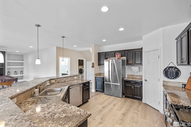 kitchen with light stone countertops, washer / dryer, appliances with stainless steel finishes, light wood-style floors, and a sink