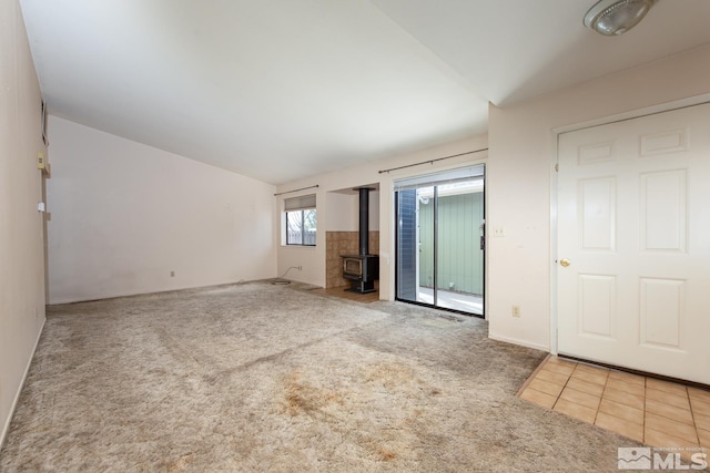 unfurnished living room with tile patterned floors, carpet flooring, a wood stove, and lofted ceiling