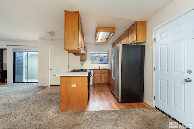 kitchen featuring brown cabinets, a sink, appliances with stainless steel finishes, light countertops, and light colored carpet