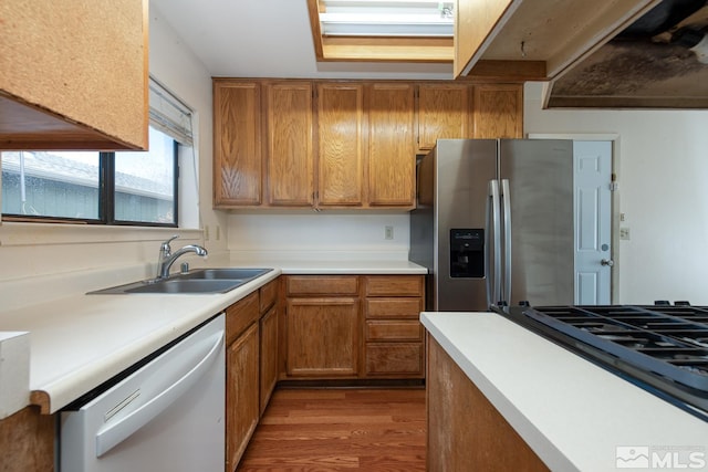 kitchen featuring wood finished floors, stainless steel fridge with ice dispenser, white dishwasher, a sink, and brown cabinets