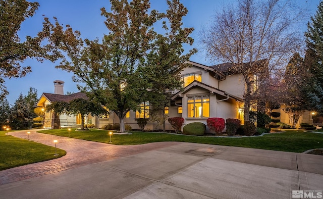 view of front facade with a front lawn, decorative driveway, a chimney, and stucco siding