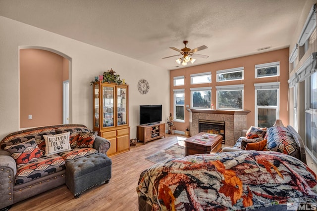 living room featuring visible vents, a tiled fireplace, a textured ceiling, wood finished floors, and arched walkways