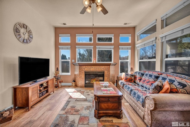 living area featuring a tiled fireplace, visible vents, a ceiling fan, and wood finished floors