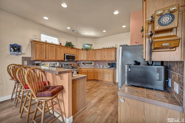 kitchen featuring light wood-style flooring, tasteful backsplash, stainless steel appliances, a peninsula, and a breakfast bar area