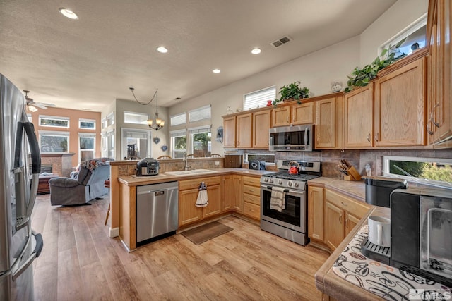 kitchen featuring visible vents, a sink, a stone fireplace, appliances with stainless steel finishes, and tasteful backsplash