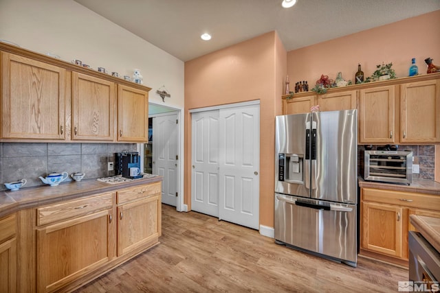 kitchen with stainless steel fridge with ice dispenser, a toaster, tile countertops, decorative backsplash, and light wood-style floors