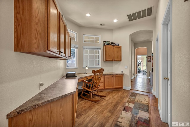 home office featuring light wood-type flooring, visible vents, arched walkways, and built in desk