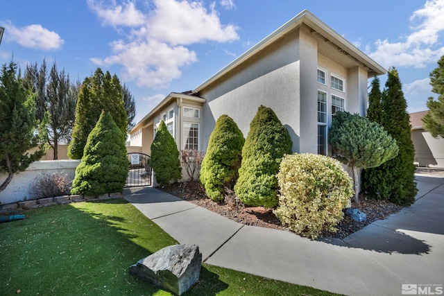 view of side of home with stucco siding, a lawn, fence, and a gate