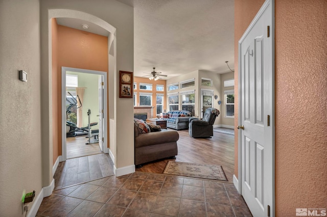 hallway featuring dark tile patterned floors, arched walkways, baseboards, and a textured wall