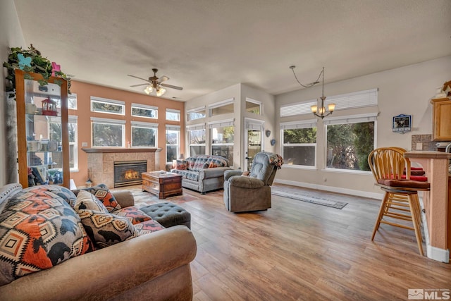 living room with a fireplace, ceiling fan with notable chandelier, light wood-style floors, and baseboards