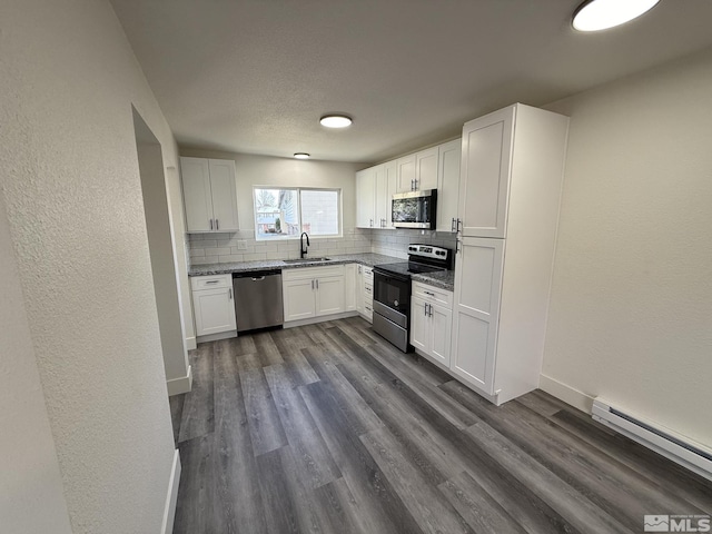 kitchen with a baseboard heating unit, decorative backsplash, appliances with stainless steel finishes, dark wood-style floors, and a sink