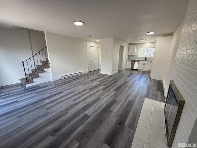 unfurnished living room featuring stairway, baseboards, dark wood finished floors, a textured ceiling, and a baseboard heating unit