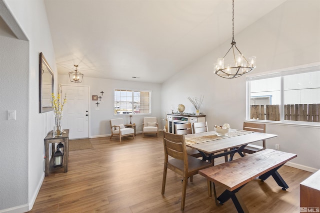 dining space with a notable chandelier, vaulted ceiling, baseboards, and wood finished floors