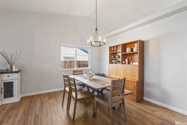 dining room with baseboards, lofted ceiling, wood finished floors, and a chandelier