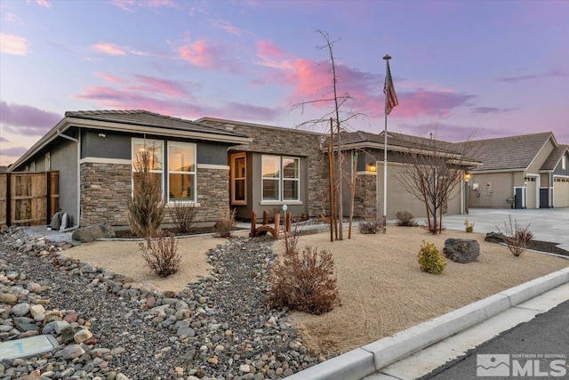 view of front of home featuring fence, an attached garage, stucco siding, concrete driveway, and stone siding