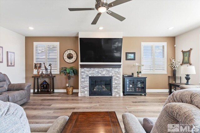 living room featuring a stone fireplace, wood finished floors, baseboards, and a healthy amount of sunlight