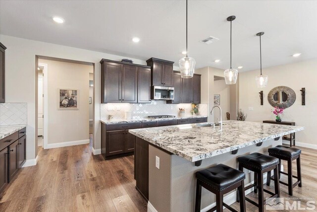 kitchen with light stone countertops, dark brown cabinetry, appliances with stainless steel finishes, wood finished floors, and a sink