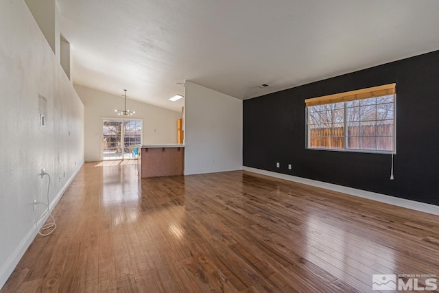 unfurnished living room with hardwood / wood-style floors, vaulted ceiling, a notable chandelier, and baseboards