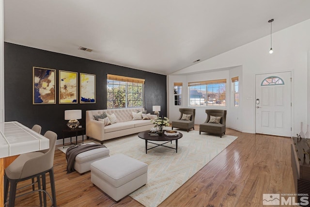 living area with light wood finished floors, visible vents, and vaulted ceiling