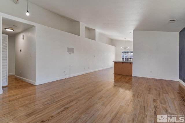 unfurnished living room with baseboards, visible vents, an inviting chandelier, lofted ceiling, and light wood-style flooring