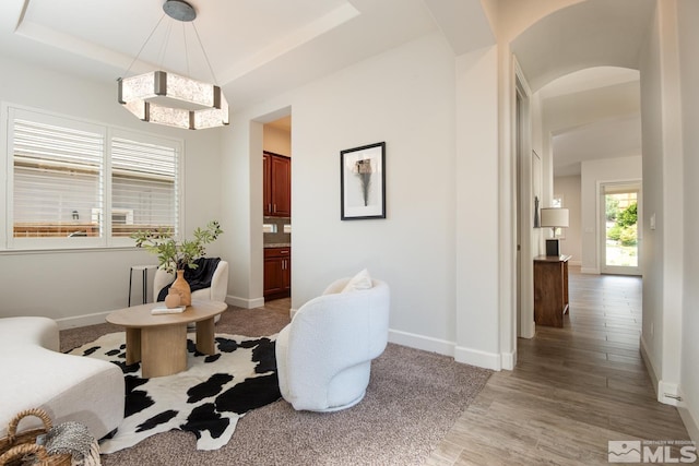 sitting room with light wood-style floors, baseboards, a raised ceiling, and arched walkways