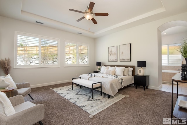 bedroom featuring multiple windows, a raised ceiling, and arched walkways